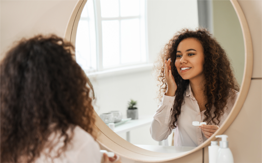 Femme qui regarde dans un miroir en insérant des lentilles dans ses yeux