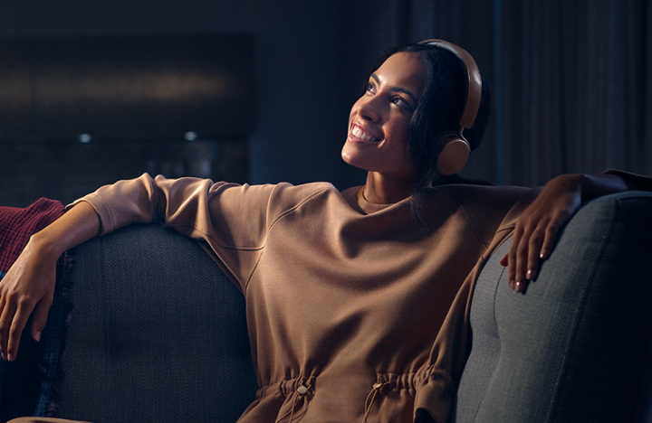 Mujer relajándose en un sofá con auriculares mirando hacia arriba y sonriendo alegremente